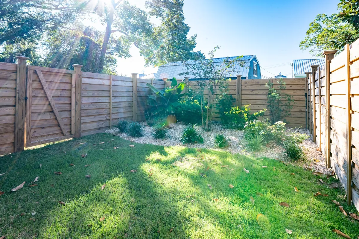 A tranquil backyard with well-maintained grass, sturdy wooden fencing, and various lush plants. The enclosed space is shaded by mature trees at the perimeter, offering a safe and peaceful outdoor environment.