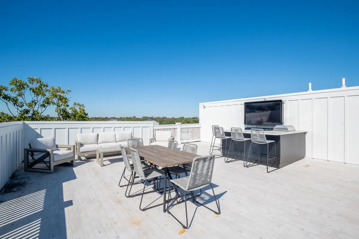 A contemporary outdoor dining area on the rooftop, with a large dining table, comfy lounge seating, and an outdoor bar equipped with a television. The setting is perfect for alfresco meals, socializing, and evening TV under the stars.