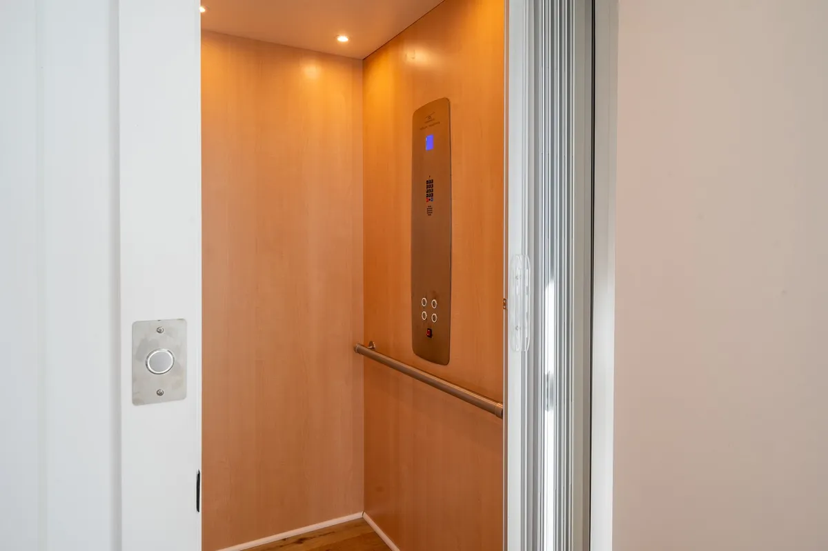 A sleek interior view of an elevator with a modern control panel, smooth wooden walls, and soft lighting, evoking efficient vertical movement within the home. The image suggests ease of access for guests with mobility needs or when carrying luggage and beach gear.