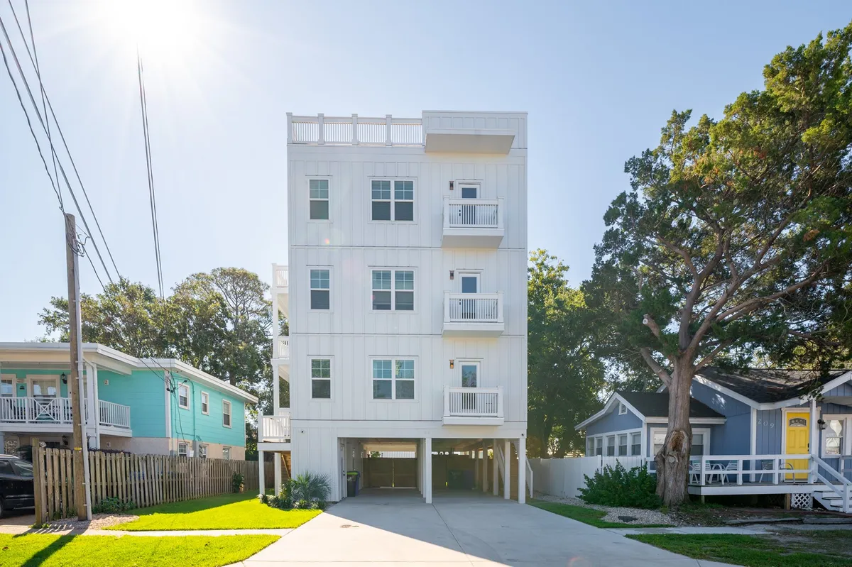 A three-story modern building with three balconies is nestled among greenery. The balconies are arranged to showcase multiple outdoor spaces for relaxation, socializing, and enjoying sunsets. The welcoming design invites group activities and reflects the home’s focus on togetherness.