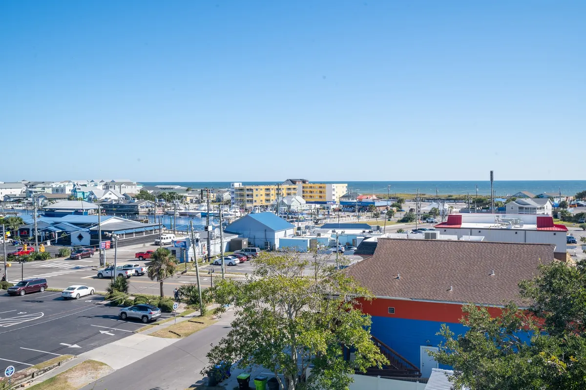 A panoramic view showcasing the nearby ocean, colorful buildings, a bustling marina, and lively street activity. The scene is vibrant and relaxed, capturing the spirit of a coastal community.